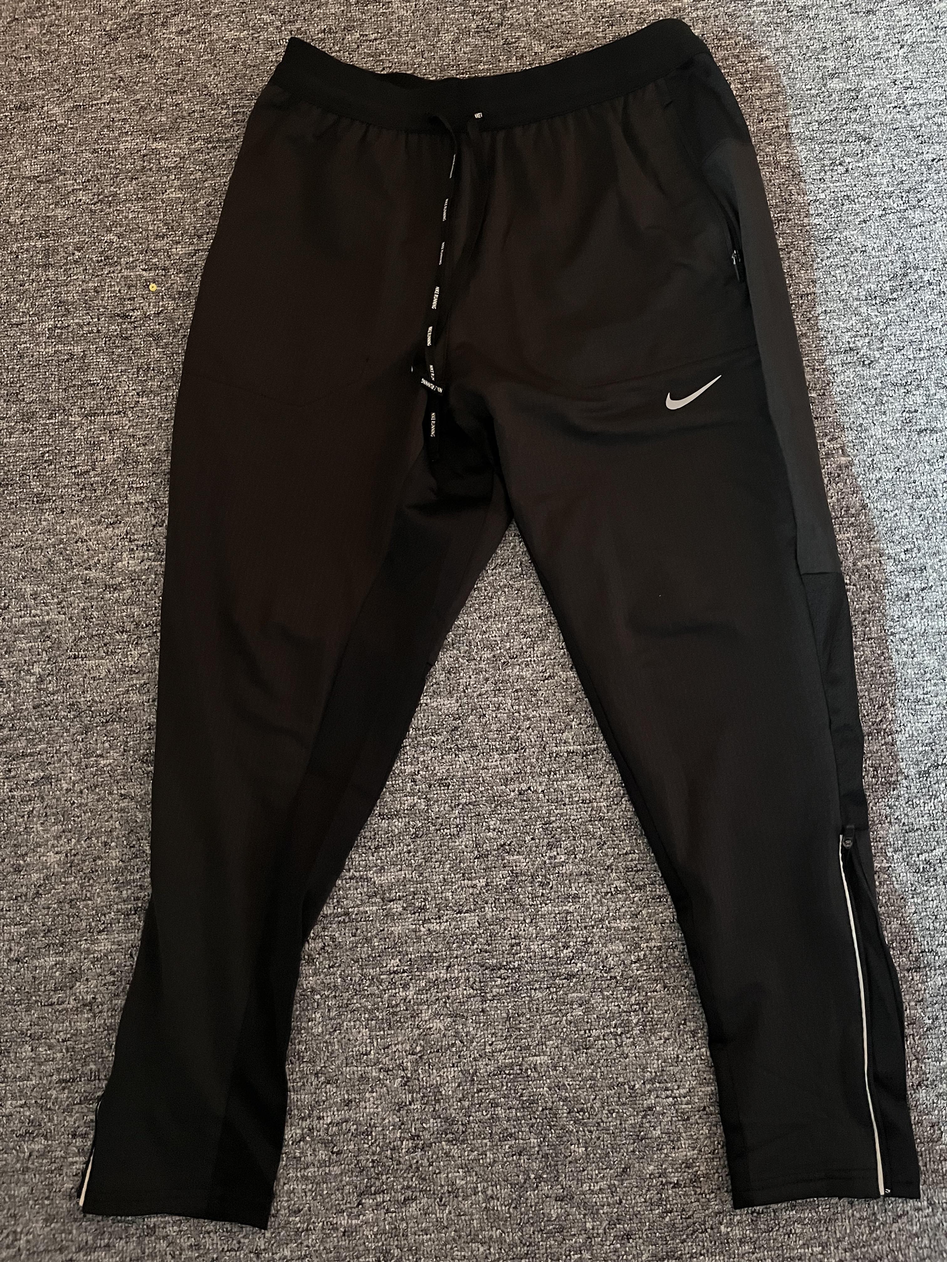 Black running pants laid flat with a drawstring waistband, zipped pockets and lower-leg zippers